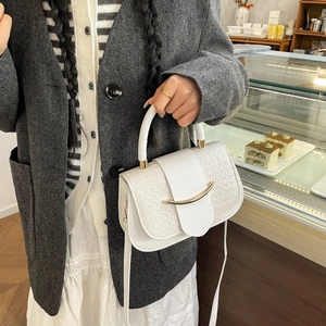 Detail of white woven texture leather handbag with gold metal clasp in a cafe setting