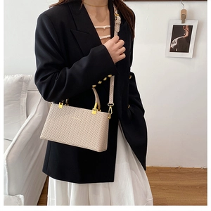 Close-up of beige woven texture bag with gold hardware worn by a model in a black blazer