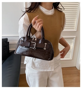 Detail of dark brown faux crocodile leather handbag with silver buckle and glossy finish