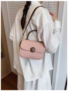 Detail of pink canvas crossbody bag with dark brown circular buckle and round handles