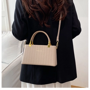 Detailed macro view of woven texture and gold metal handle on beige box crossbody bag