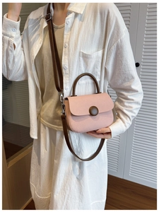 Detail view of pink crossbody bag with vintage round buckle and brown handle handle detail