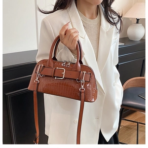 Close-up of brown crocodile texture shell bag with metallic buckle and slim shoulder strap