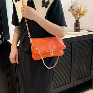 Bolso de hombro de cuero naranja con cadena dorada usado por una modelo mujer