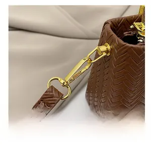 Close-up of golden metal hook and woven strap detail on brown faux leather handbag