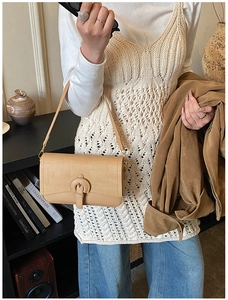 Detail of tan textured shoulder bag with vintage metal V-clasp on artistic background
