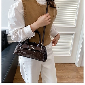 Detail of dark brown faux crocodile leather bag with belt buckle and glossy finish