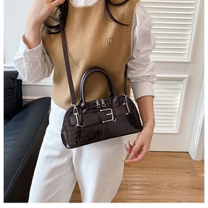 Detail of dark brown croc-effect shell bag with shiny finish and metal buckle strap