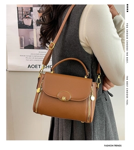 Detail view of brown lychee grain leather handbag with gold M logo and side zippers