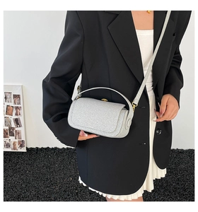 Sac à main argenté pailleté avec fermoir doré porté par un mannequin en décor moderne