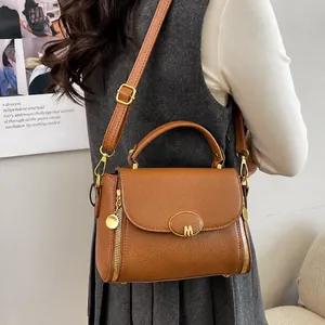 Detalle de bolso clásico de cuero marrón con hebilla M dorada y acabado texturizado