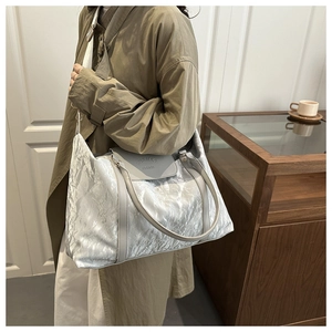 Detail of metallic silver pleated travel bag with gray leather handles and logo flap