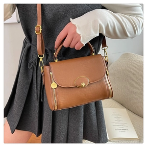 Detailed view of brown litchi pattern leather handbag with gold M-buckle on a model