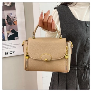 Detail of beige hobo bag with pebble leather texture and gold M hardware on flap