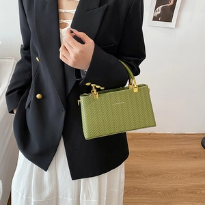 Green woven texture box bag with gold handles carried by model in casual chic outfit
