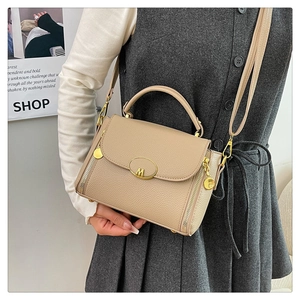 Detail of beige pebbled leather handbag featuring gold M hardware and slim shoulder strap
