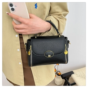 Close-up of black lychee grain leather handbag with gold M-logo and metallic pendant