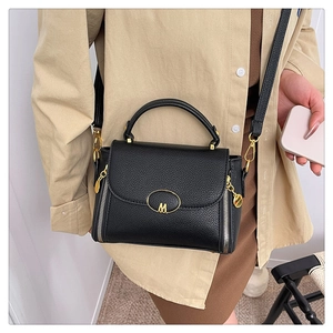 Detailed shot of black lychee leather handbag with M logo and adjustable shoulder strap