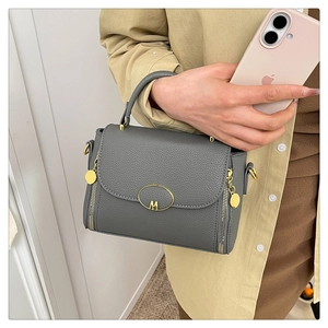 Close-up of grey litchi grain leather handbag with gold M-logo buckle and side zippers