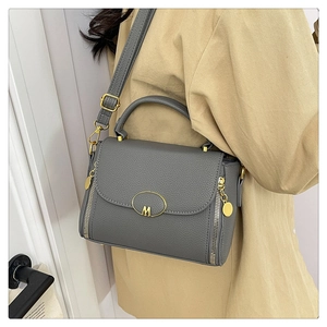 Detail of grey lychee leather handbag with gold M-logo buckle and side zipper accents