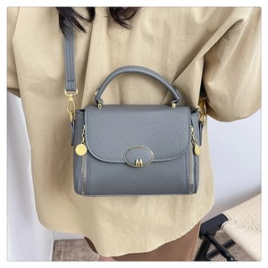 Detail of grey pebble leather crossbody bag with gold M-logo and side zipper accents