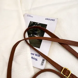 Detalle de la correa ajustable de cuero marrón con hebilla dorada sobre fondo blanco