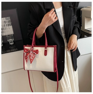 Detail of white snakeskin tote bag with red leather trim and silk heart bow charm