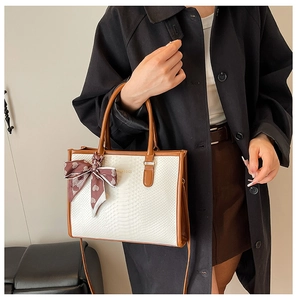 Detail of white tote bag with snake texture, brown leather trim, and heart silk scarf