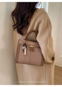 Detail der braunen Hahnentritt-Handtasche mit Holzperlen-Anhänger und goldener Aufschrift