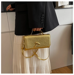 Detail of gold woven baguette bag featuring an artistic metallic twist knot clasp on the flap