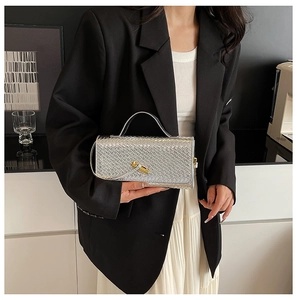 Detail of silver woven handbag with golden bamboo twist lock held by model in black blazer