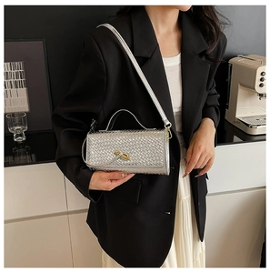 Silver woven baguette bag with metallic lock shown on a stylish model in a modern cafe setting
