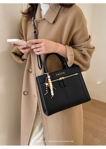 Detail of black faux leather handbag featuring golden logo and wooden beaded tassel