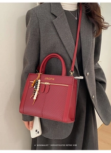 Detail der burgunderroten Handtasche mit Fischgrätenmuster und Perlenanhänger-Dekor