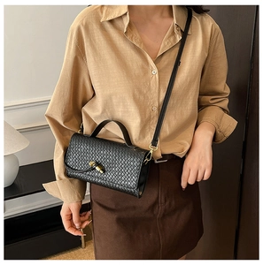 Detailed view of a black woven crossbody bag with gold twist lock on a stylish model