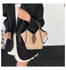 Detail of a crinkled beige bucket bag with dark brown handles and golden hardware
