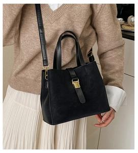 Detail of matte black bucket bag with gold metal buckle shown on shoulder