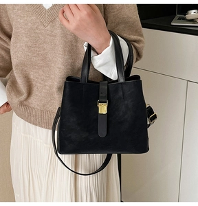 Detail of black semi-matte bucket bag with gold buckle and adjustable strap on model