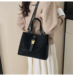 Detail of black matte leather tote bag with gold metal buckle and vertical strap accent