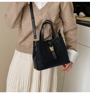 Detail view of the black textured bucket bag with gold clasp shown on a model