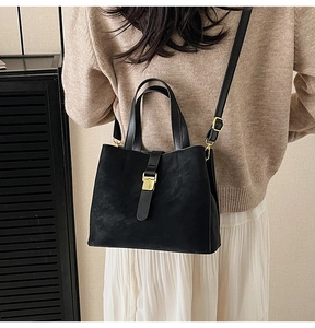 Detail of black suede bucket bag with gold buckle and adjustable strap on a model