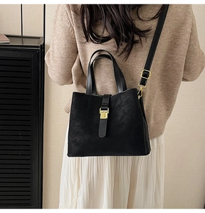 Detail of black leather bucket bag featuring gold metal buckle and adjustable shoulder strap