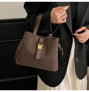 Detail of dark brown bucket bag with matte texture and gold buckle on black background