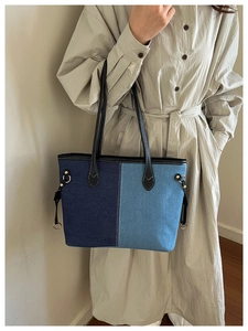 Detailed close-up of blue denim patchwork tote bag with black leather straps and gold rings