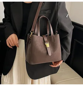 Detailed view of brown bucket bag with matte texture and golden buckle on model