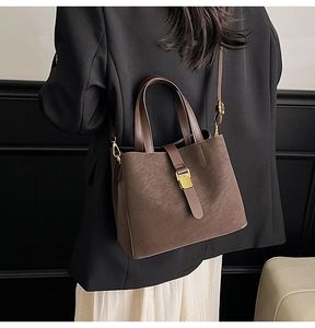 Close-up of matte brown leather tote bag with gold metal buckle and dual strap design