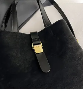 Detail of black pebbled leather bucket bag featuring a light gold metal buckle closure