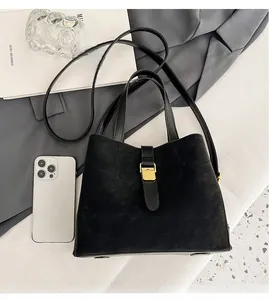 Detail of black suede bucket bag with gold buckle and smartphone for size reference