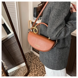 Detail of brown saddle bag with golden metal ring handle and fashion text engraving