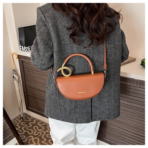 Brown leather saddle bag with ring handle and crossbody strap worn in a home setting